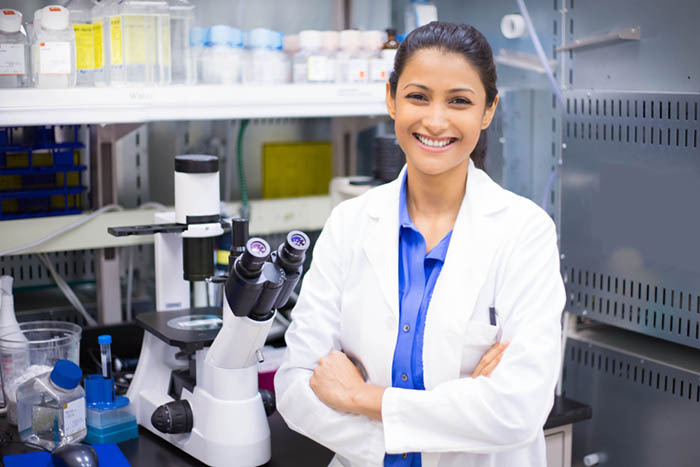 A female scientist stands in from of a microscope in a lab.