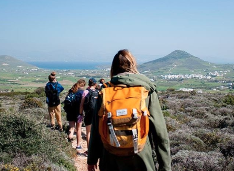 Students wearing backpacks hike along a path with a mountain in the background.