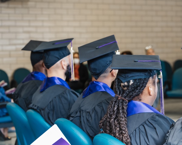 Graduates of the Emerson Prison Initiative sit facing away from the camera, wearing their graduation caps and gowns