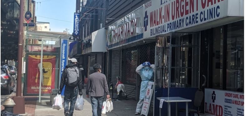 Two people with shopping bags walk down street passed closed shops past person in full body PPE