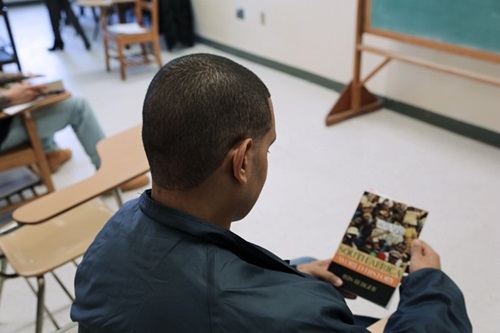 Black student sits at desk holding a book in front of them.