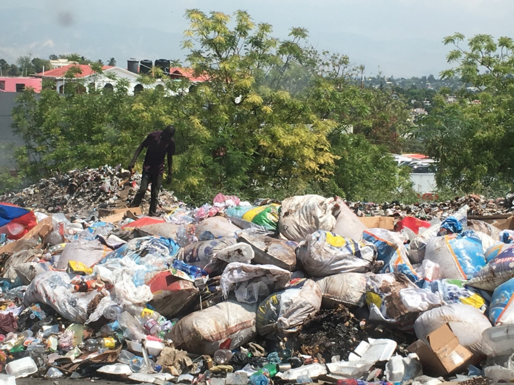 Black man walks over mountain of trash looking for recycling goods in Port-au-Prince, Haiti