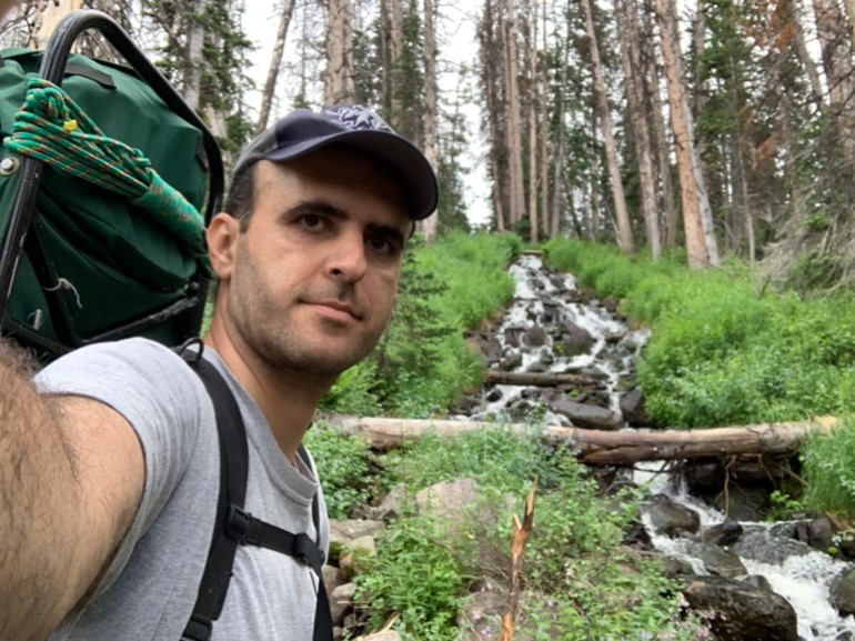 Abdehaleem Khader in foreground with backpack, forest and stream running in background