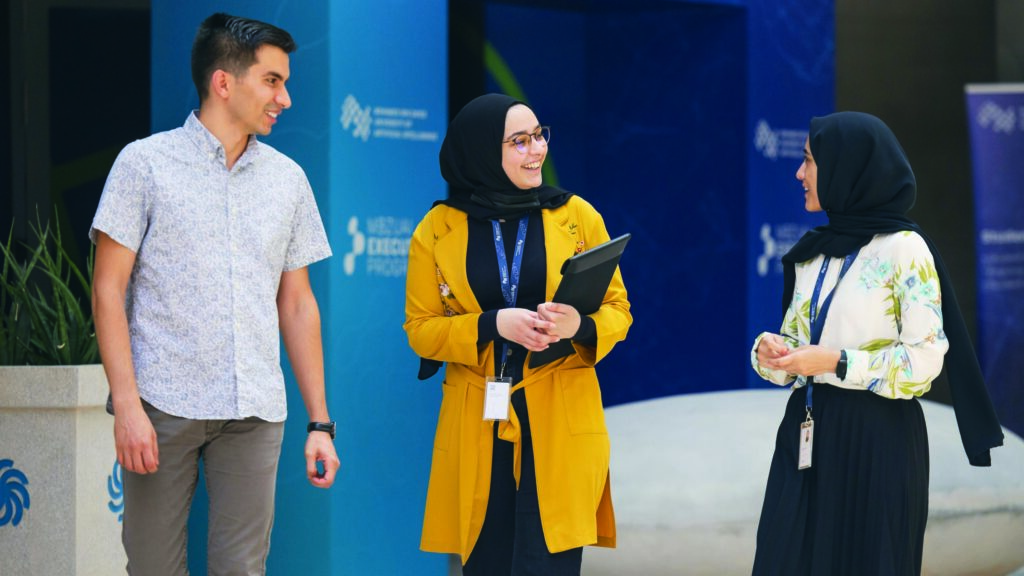 MBZUAI image of man and two women standing, talking, smiling