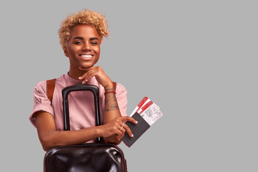 Younf person standing with luggage holding their passport that tickets are sticking out of.